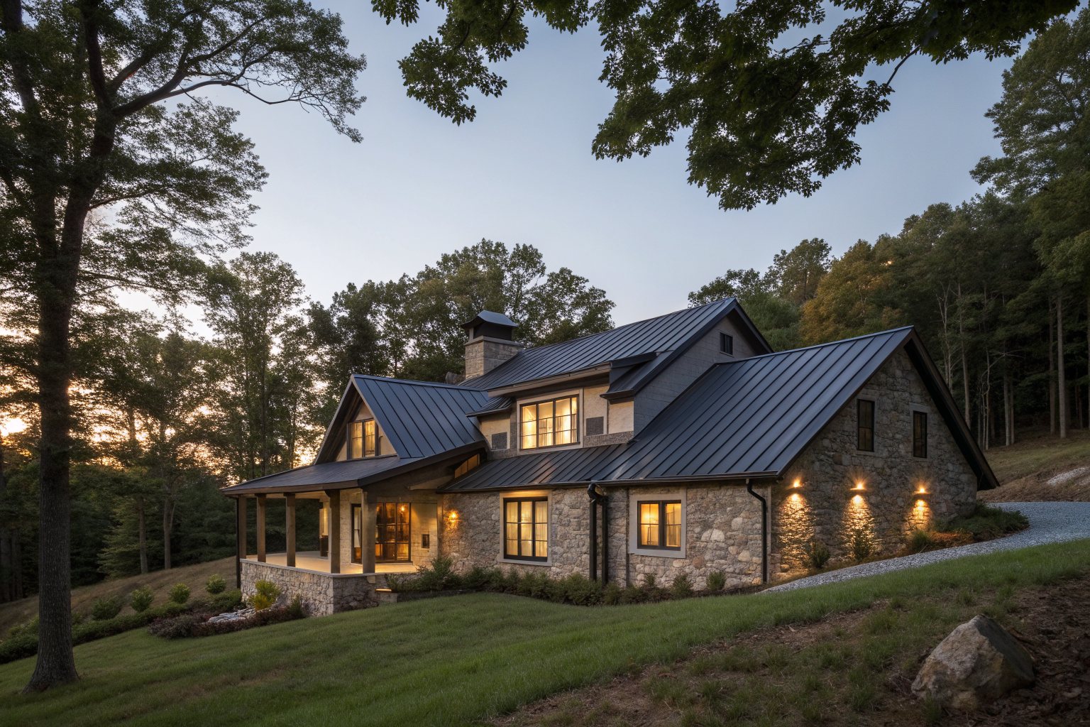 A large stone home with a dark standing-seam metal roof among trees at dusk